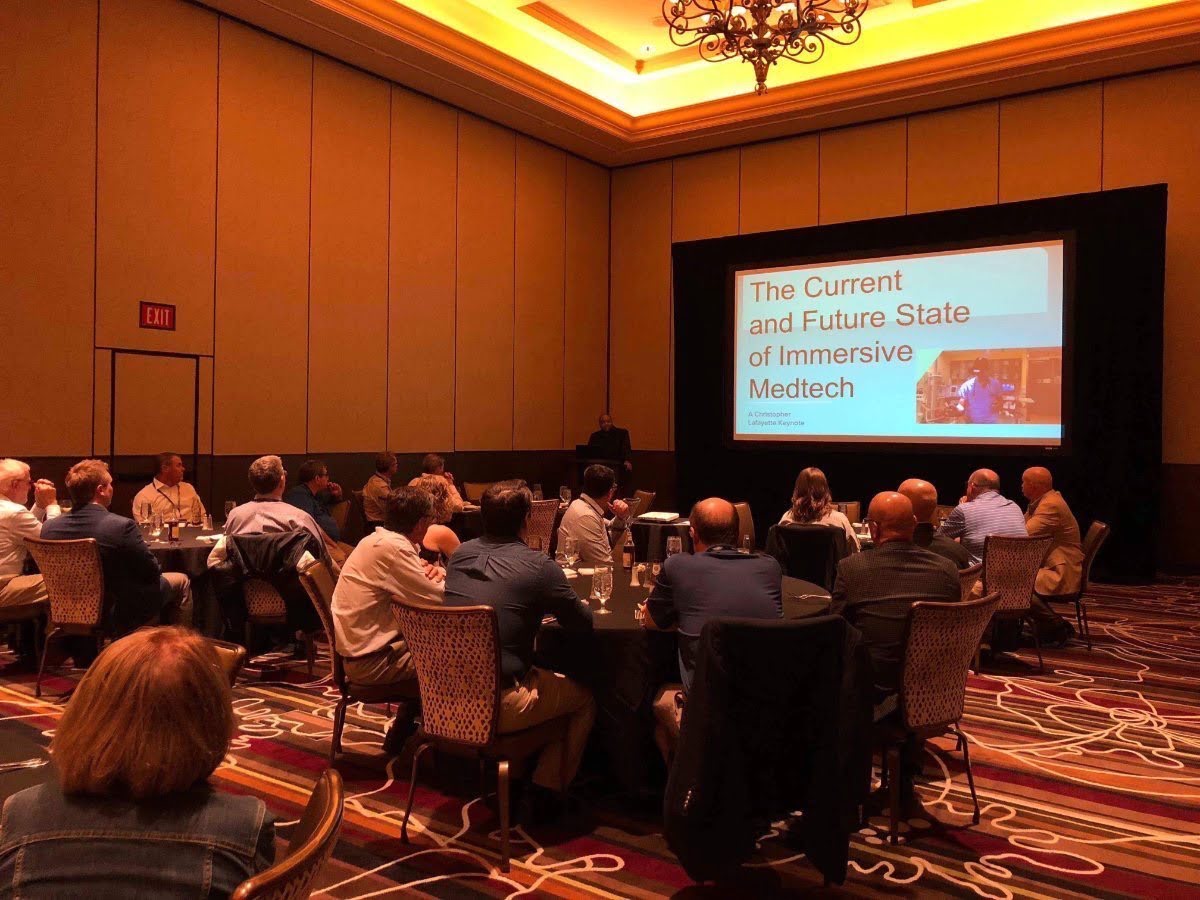 Attendees seated at round tables watch an immersive medical technology keynote in a Las Vegas conference room.