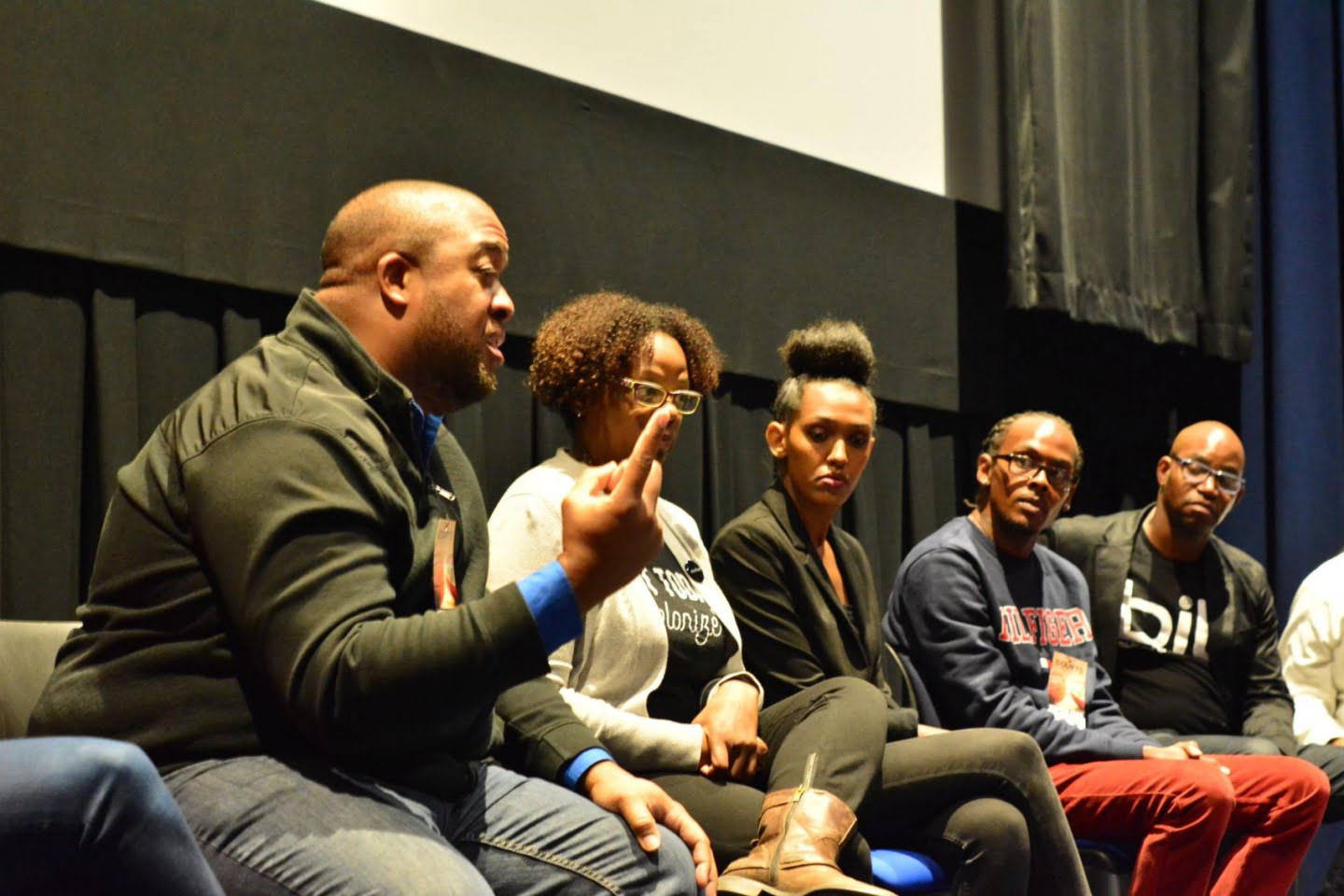 Christopher Lafayette speaks into a microphone while seated with panelists on stage.