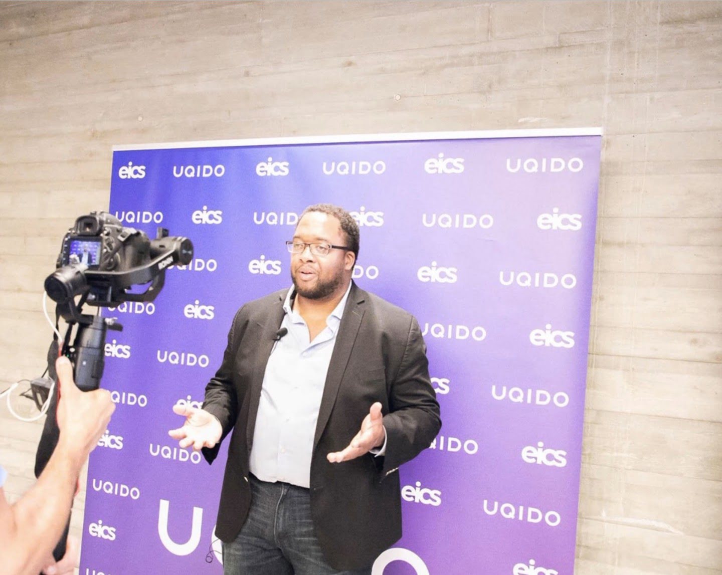 Christopher Lafayette is filmed speaking in front of an EICS backdrop.