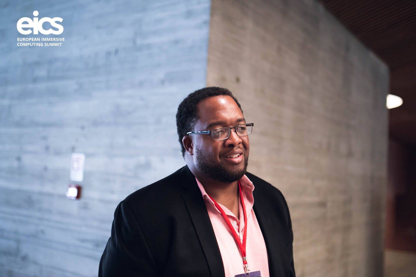 Portrait of Christopher Lafayette wearing glasses and a jacket in an EICS venue.