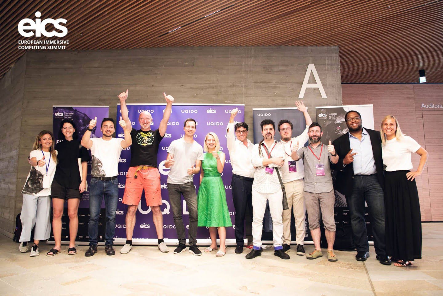Conference attendees raise their hands for a group photograph in front of the EICS backdrop.