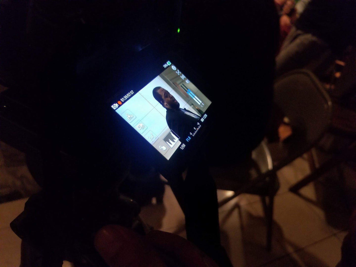 A monitor displays a remote conversation in a darkened gathering space.